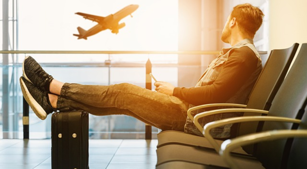 A guy watches a jet taking off with his feet up on a small suitcase