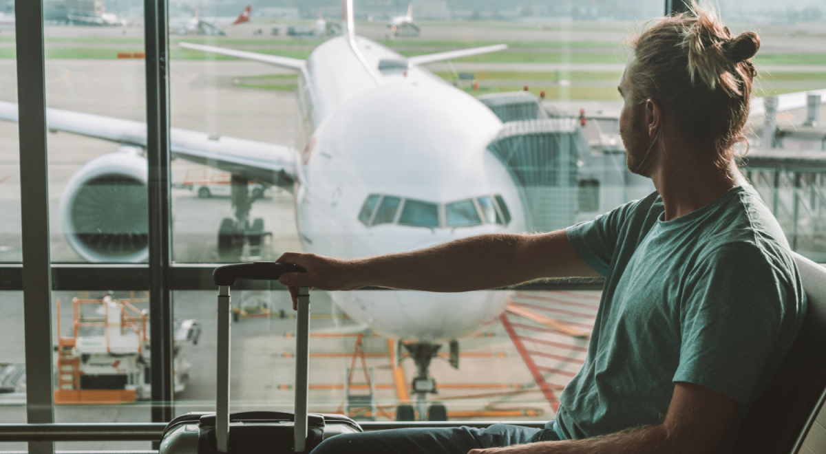 Man at airport watching plane on tarmac outside window