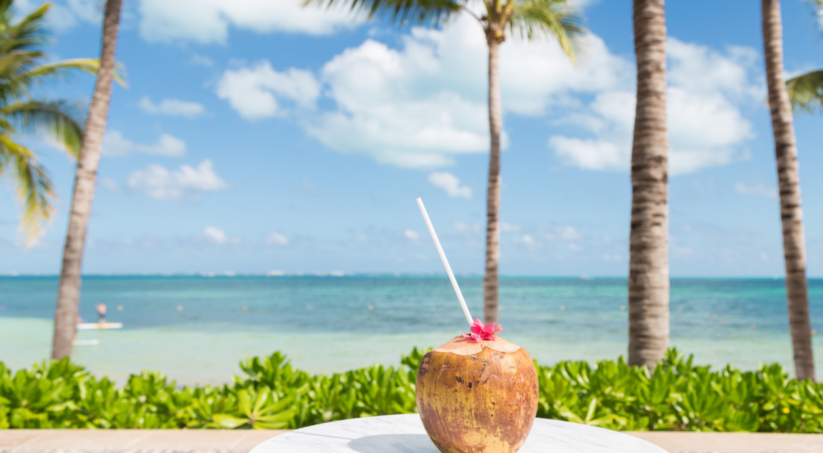 A coconut with a straw sitting on a table at a tropical beach