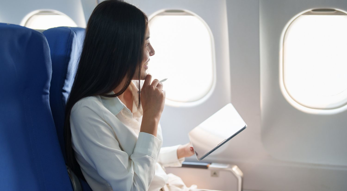 lady holding Ipad and pen under her chin looking out window of plane from business class