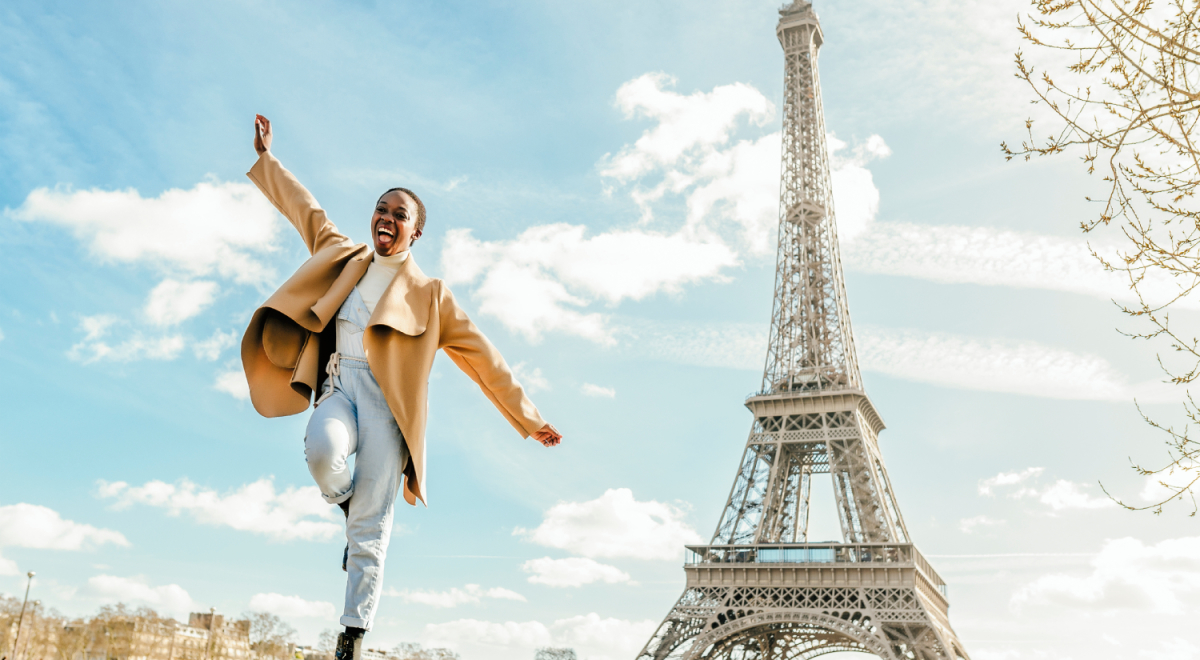 Happy young woman in front of Eiffel Tower, Paris, France - Getty Images