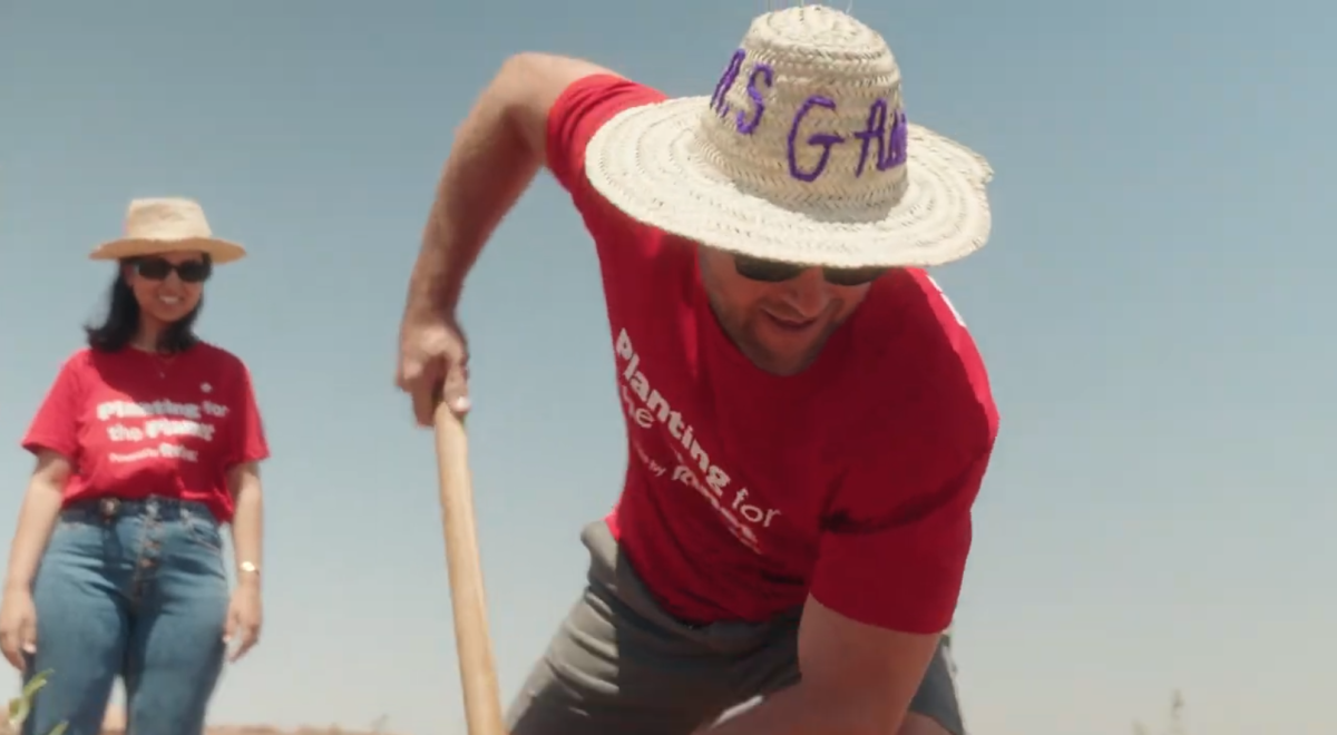 A person in a red shirt holding a shovel and digging into the ground.