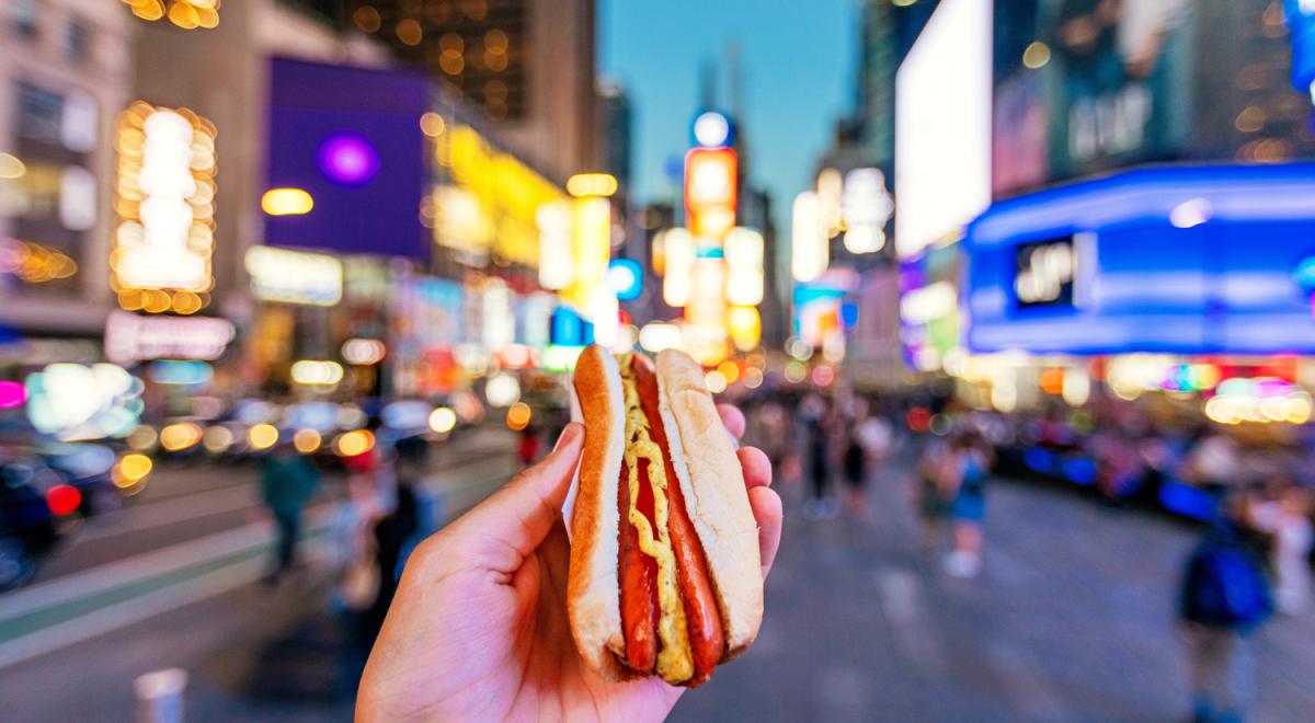 hand holding hot dog with blurred times square in background