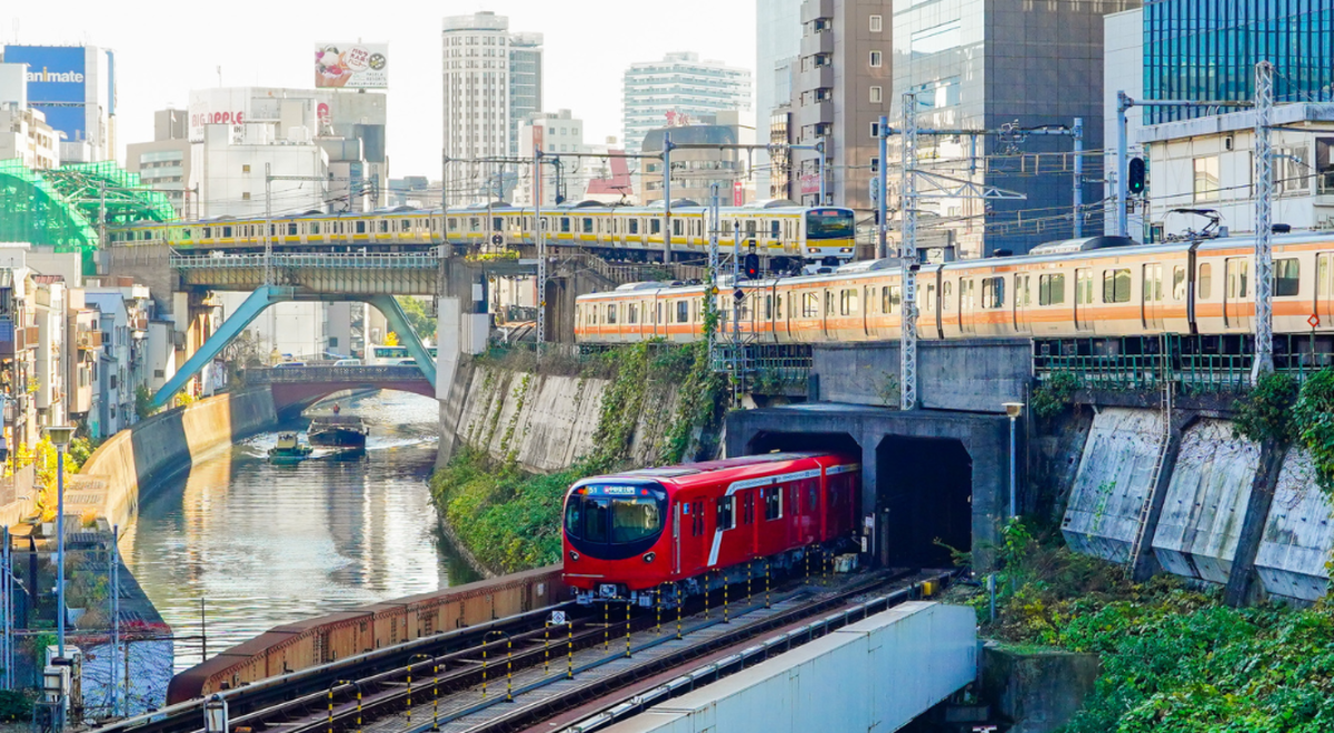 Red train driving out of tunnel while two yellow trains drive on bridges over the city