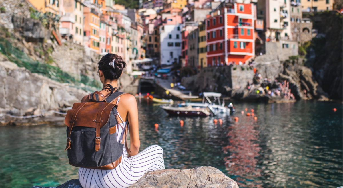 lady sitting on a rock by the water looking at coastal town in Italy