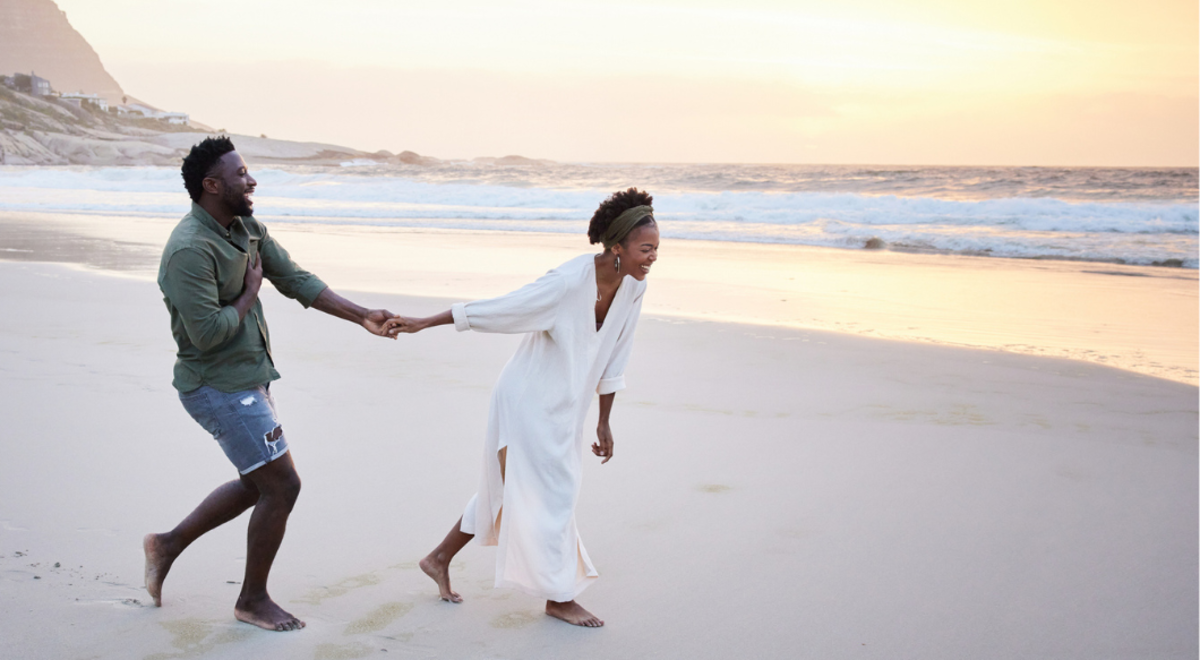 Couple running and laughing while holding hands on beach at sunset