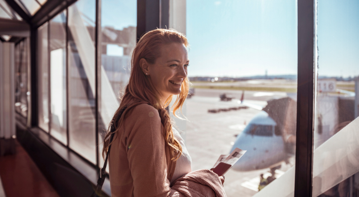 female traveller standing at window in airport smiling