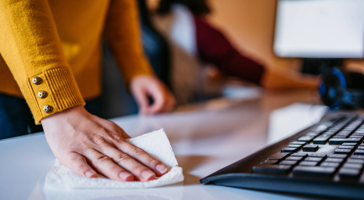 woman wearing yellow sweater wiping down desk with paper towel
