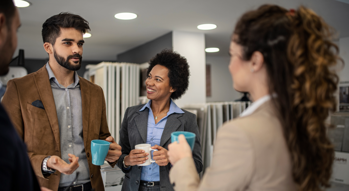 four business people each holding a cup of coffee and talking to each other in an office