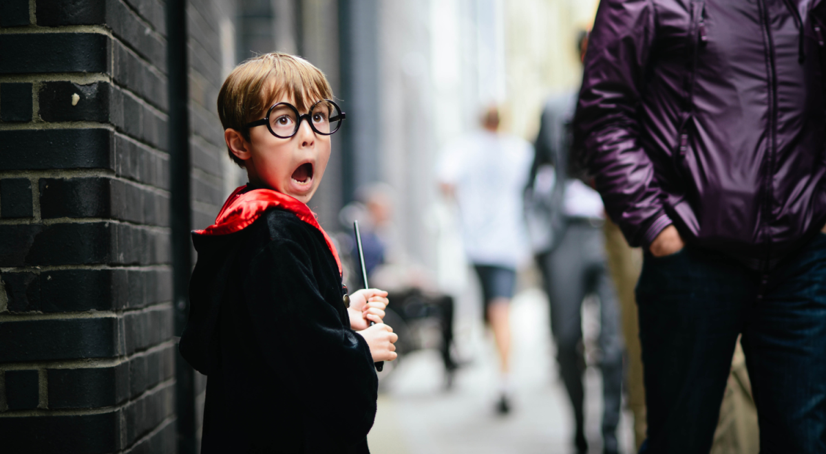 Kid dressed as harry potter holding wand and looking scared