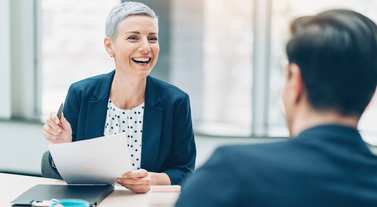 two business people looking at each other laughing while one is holding paper