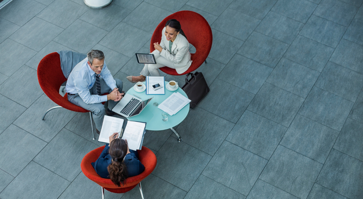 three business people sitting around coffee table in red seats