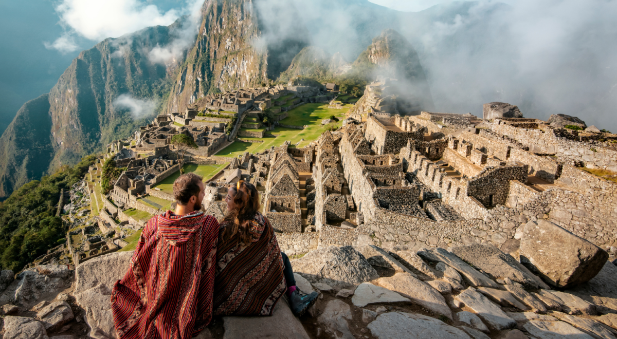 couple sitting on cliff overlooking macchu picchu peru