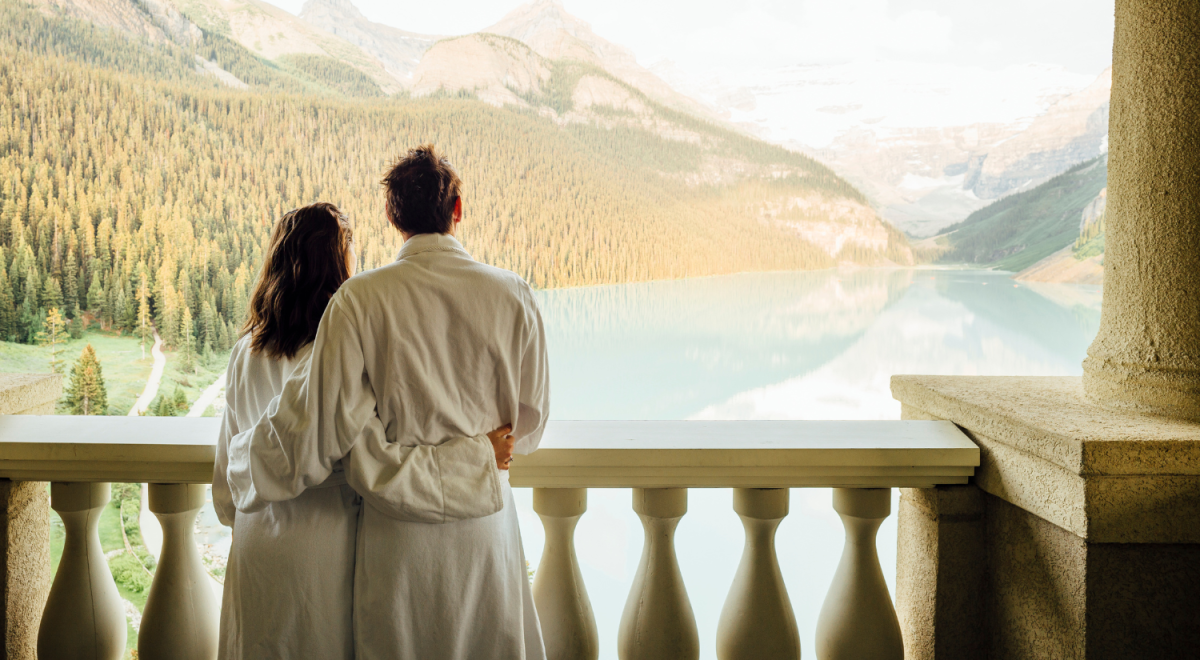 couple standing on balcony in bath robes overlooking mountains and lake in canada