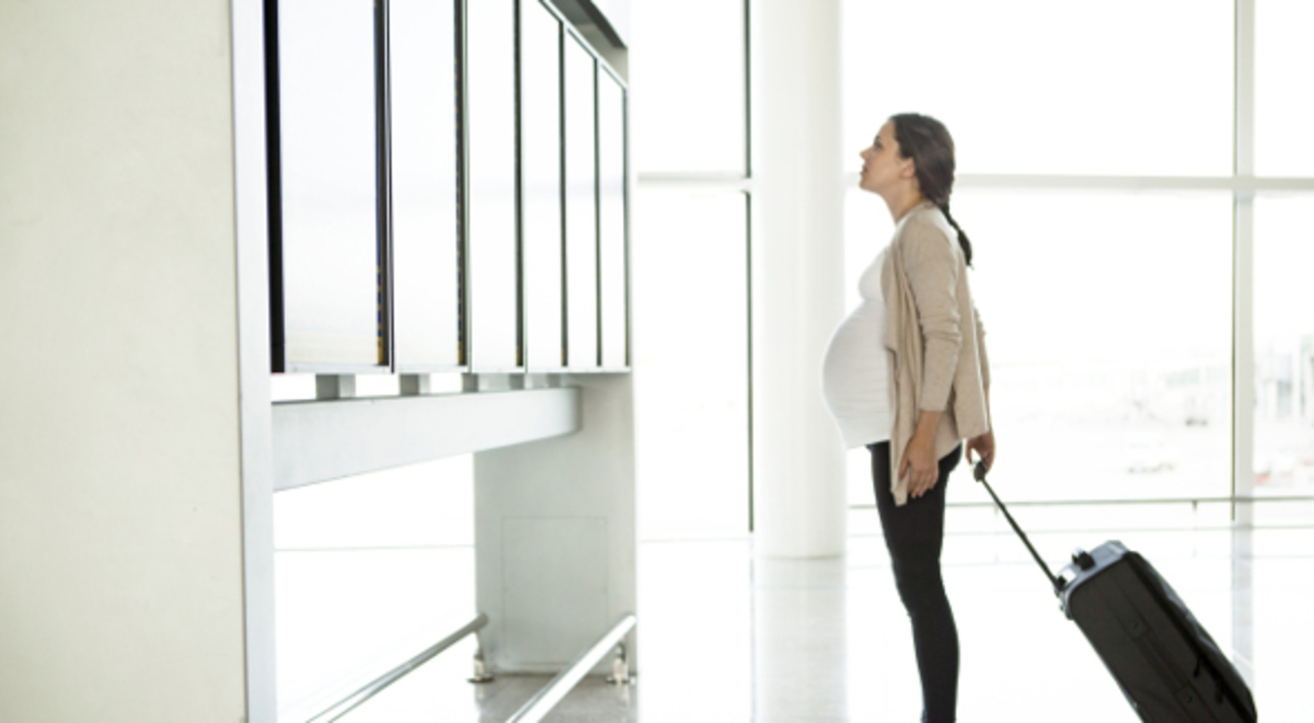 Pregnant woman waiting at the airport with her suitcase 