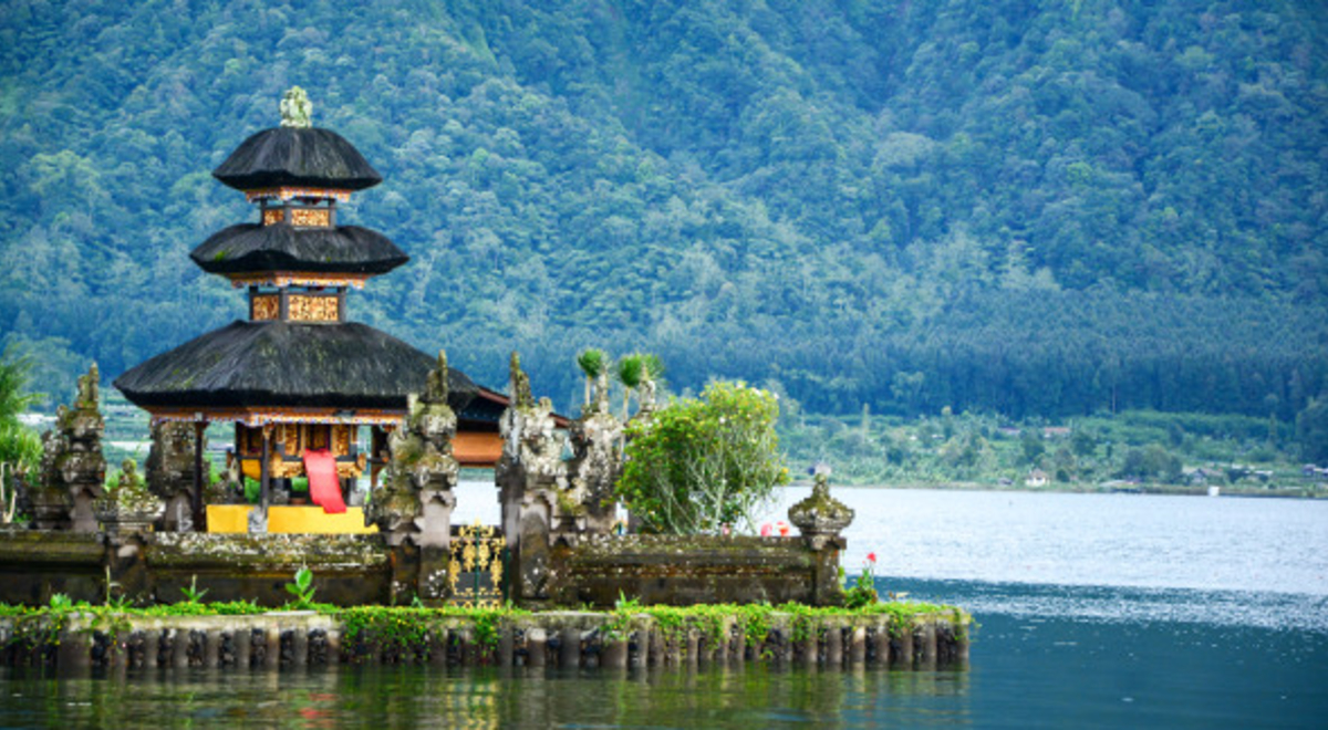 A traditional Balinese building next to a lake and mountains 