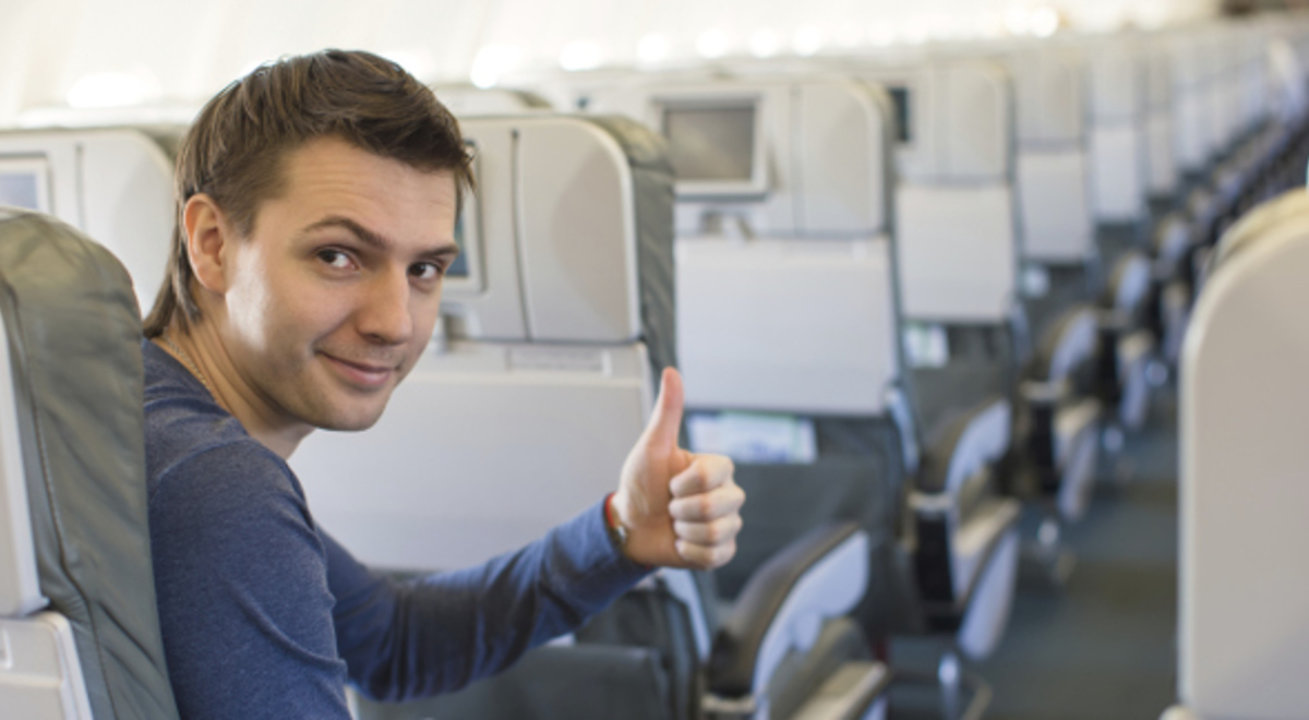 a guy in blue sweaters smiling while giving a thumbs up for a good service on the plane