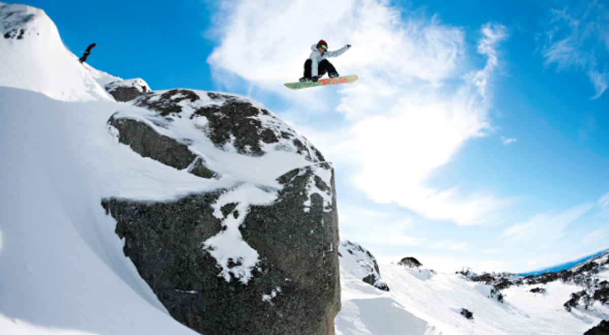 Person snowboarding over a huge rock