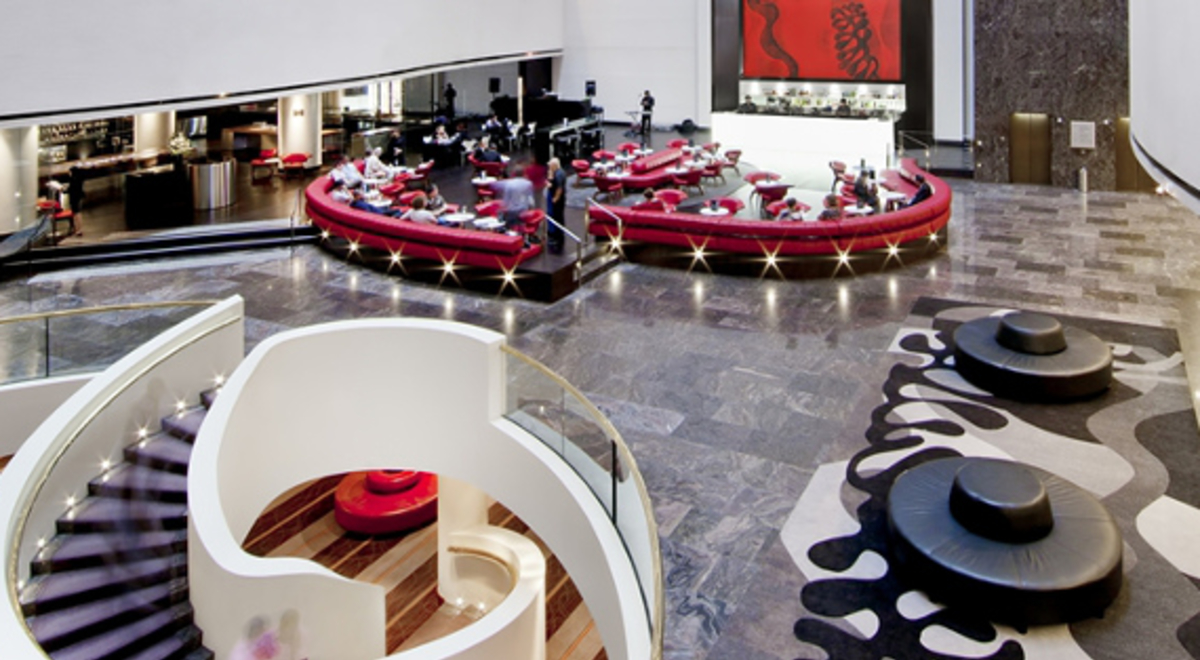 a fancy hotel restaurant with people eating on rounded red couches and waiters serving them