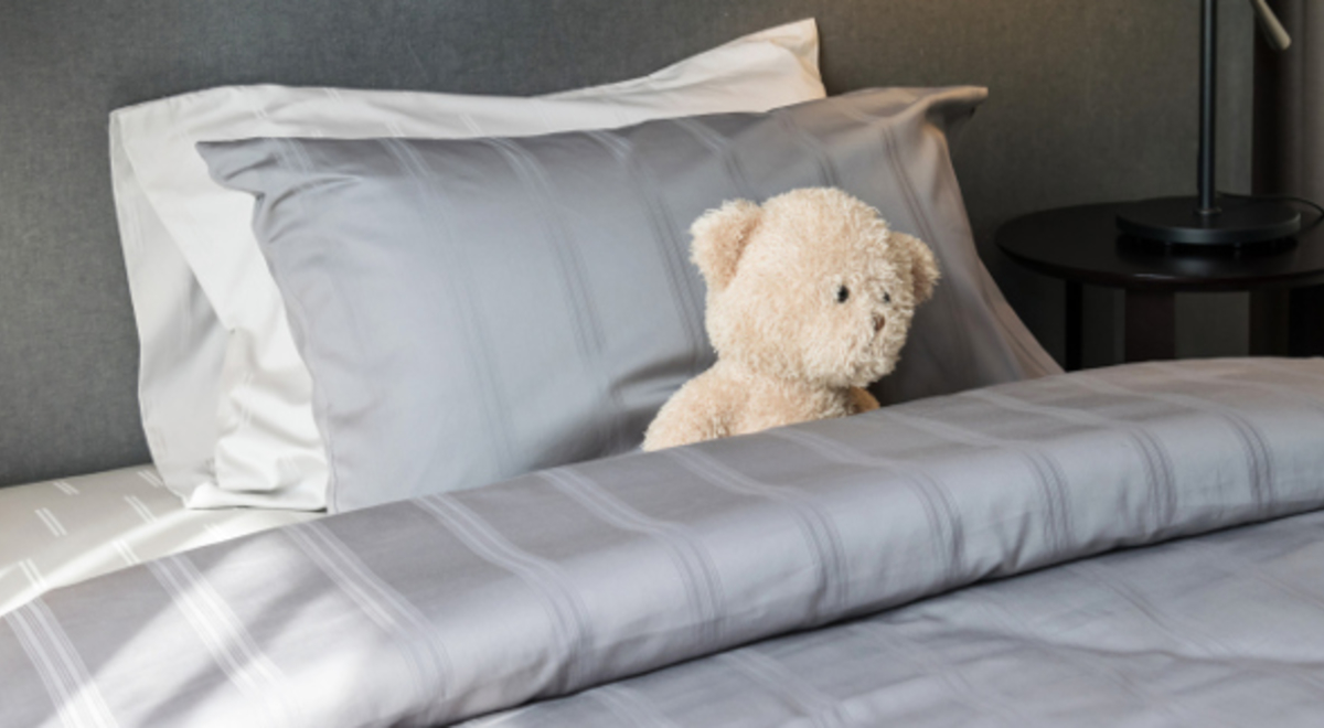 a teddy bear sitting on a king sized bed with white and silver pillow covered in silver beddings 