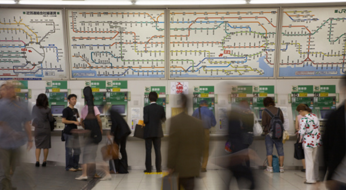 People moving in a busy public transport station in front of a colour-coded map