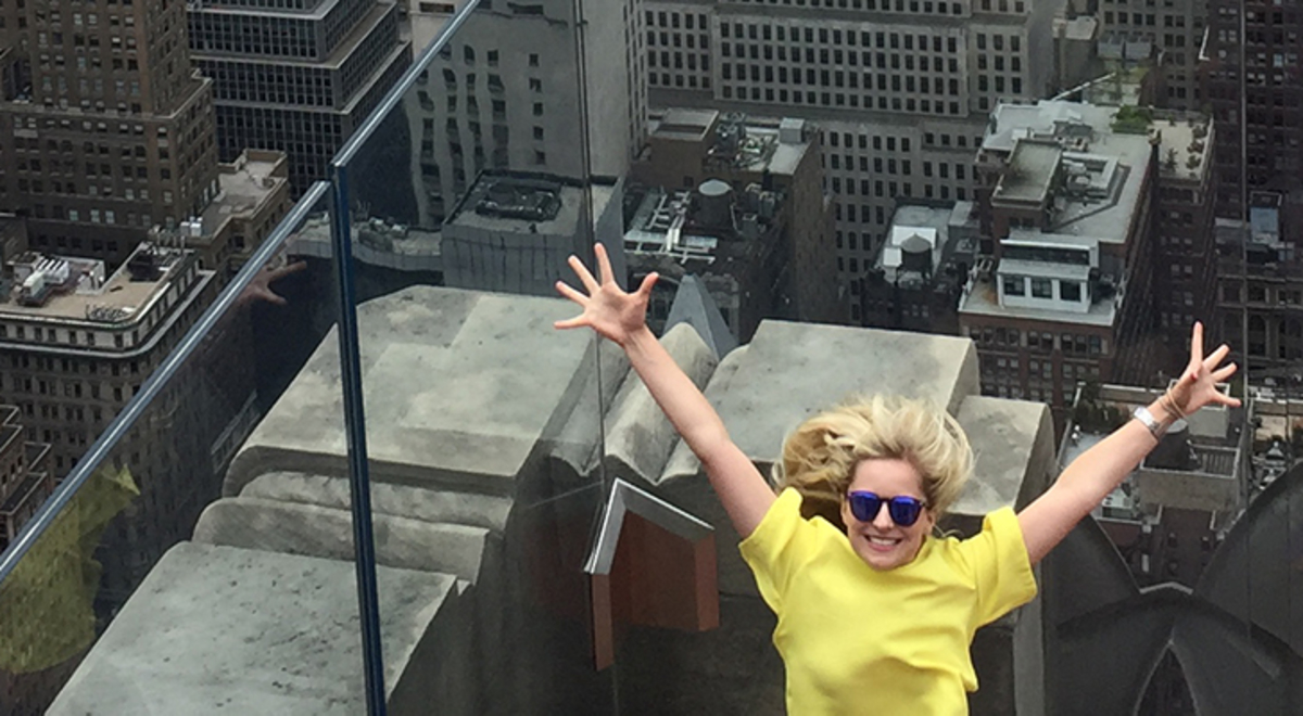 Girl in yellow shirt with her arms up in front of New York buildings 