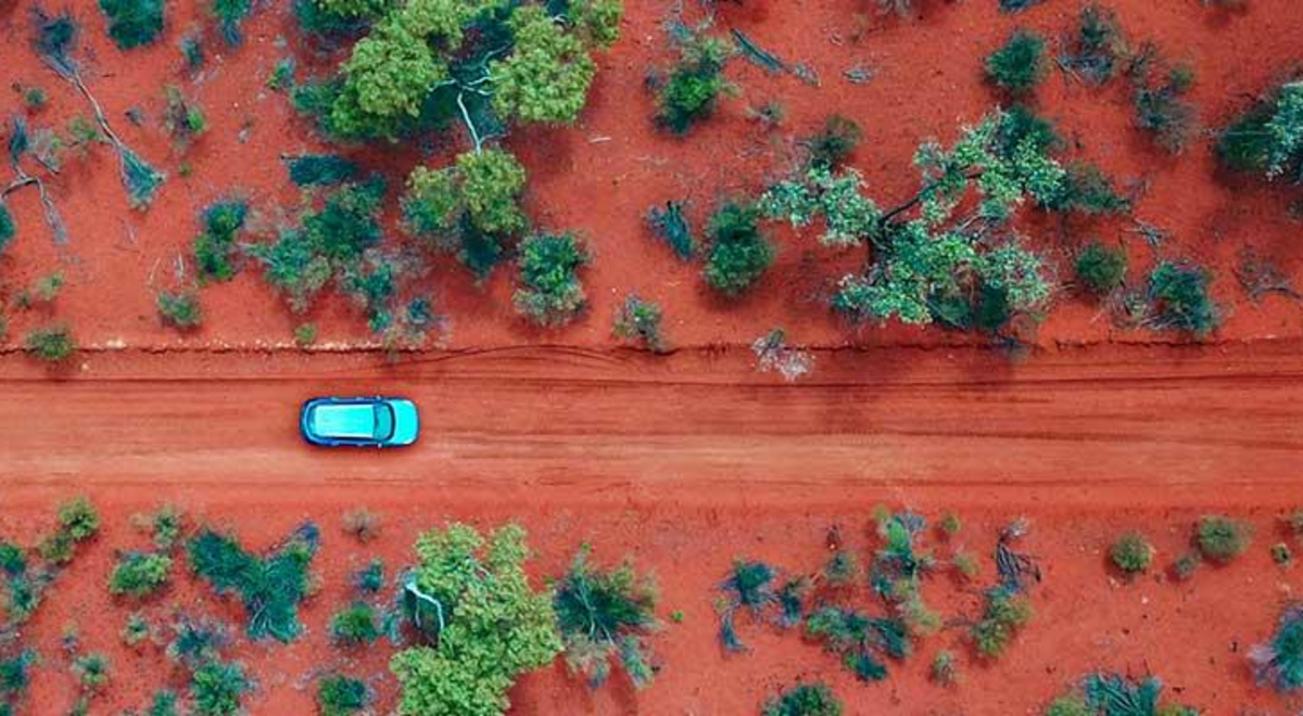 Car driving through the red roads of Alice Springs surrounded by green trees