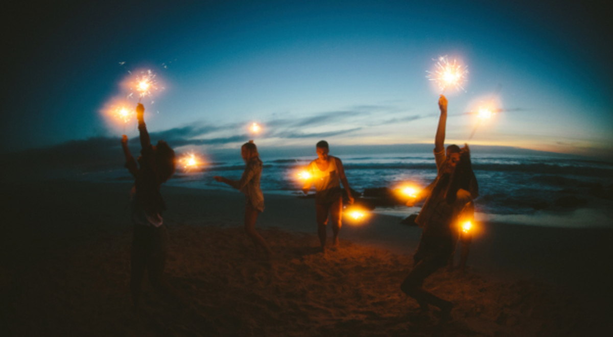 friends happily lighting firework sparklers on the beach at night