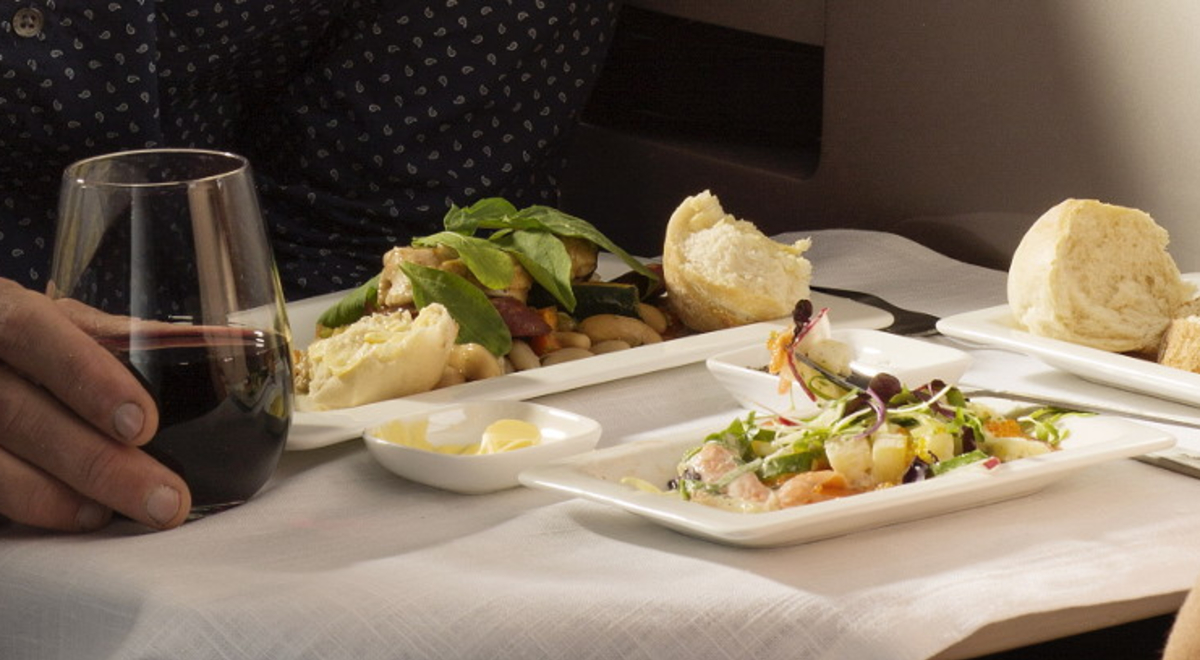 a person enjoying a fancy chicken salad meal and a glass of red wine while on his flight