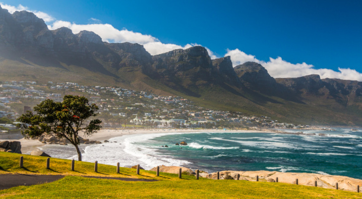 a serene view of the blue waters, green meadows, and mountainous background of the Camps Bay