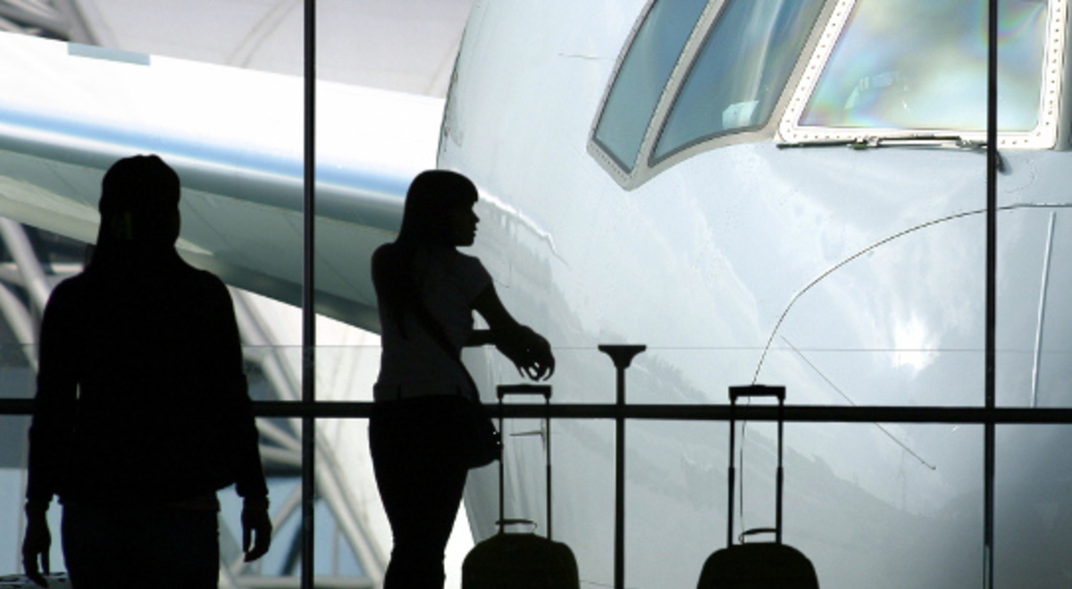 A silhouette of two women and their luggage staring through the glass window in the airport