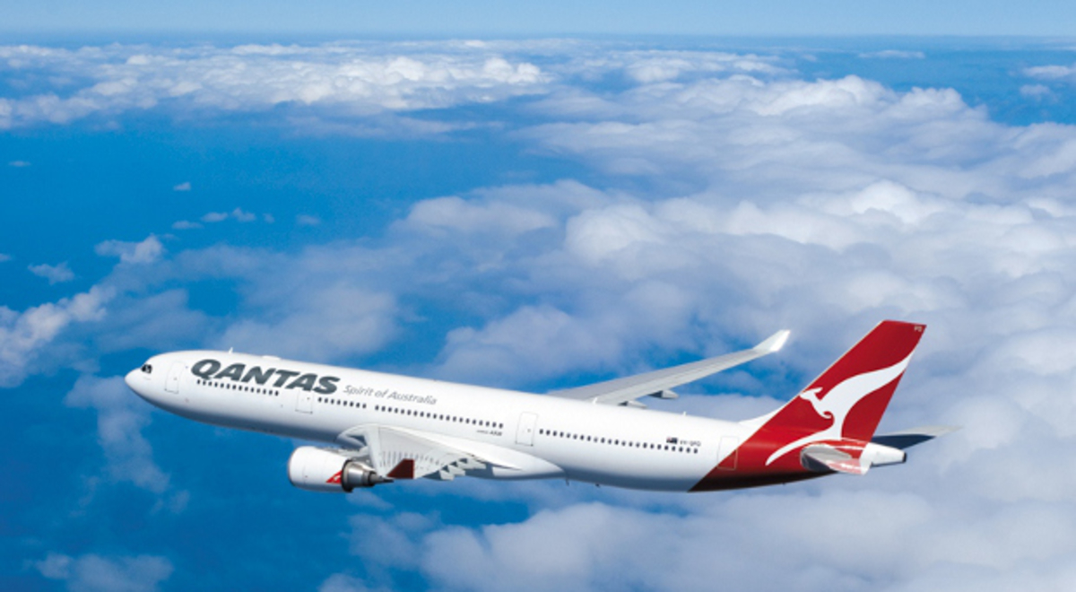 Qantas plane flying through a blue sky with scattered clouds