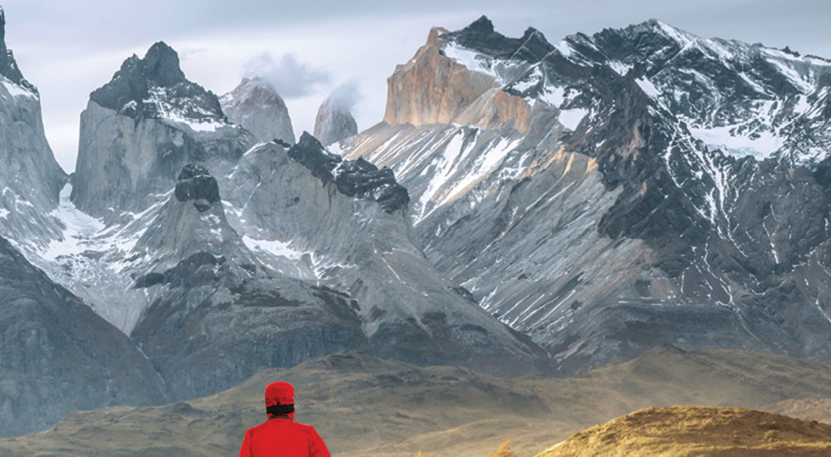 Man in a red winter coat gazing over the snowcapped mountain