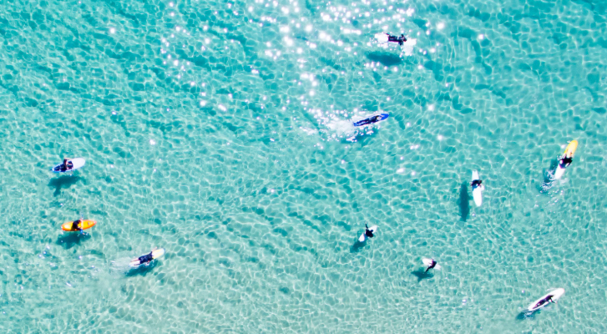 Aerial view of surfers on clear blue beach waters.