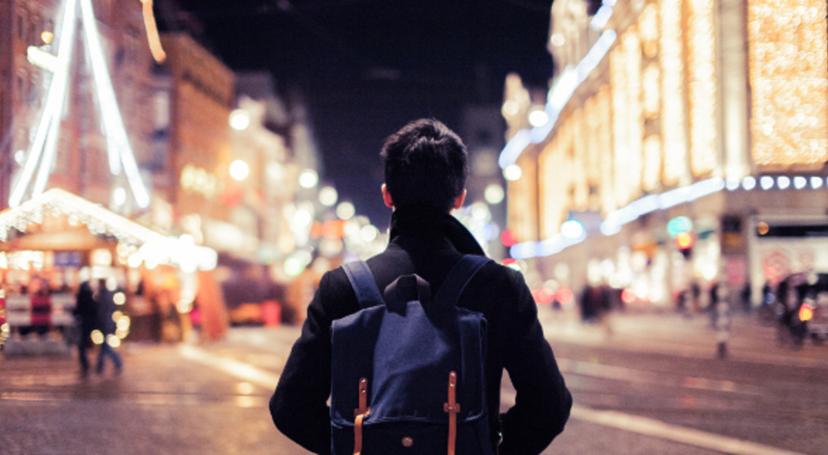 a guy with blue backpack traveling alone in the midst of a vibrantly lit city street