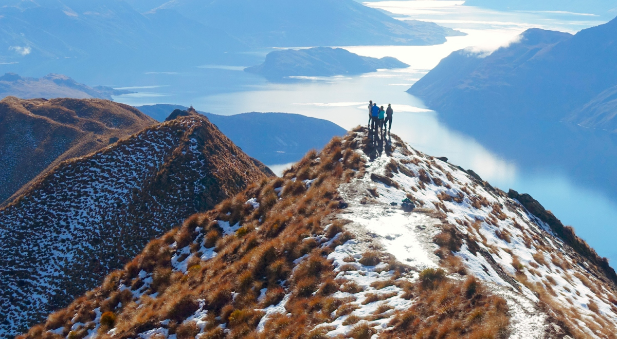 Distant view of hikers standing on a cliff against lake during winter, Queenstown