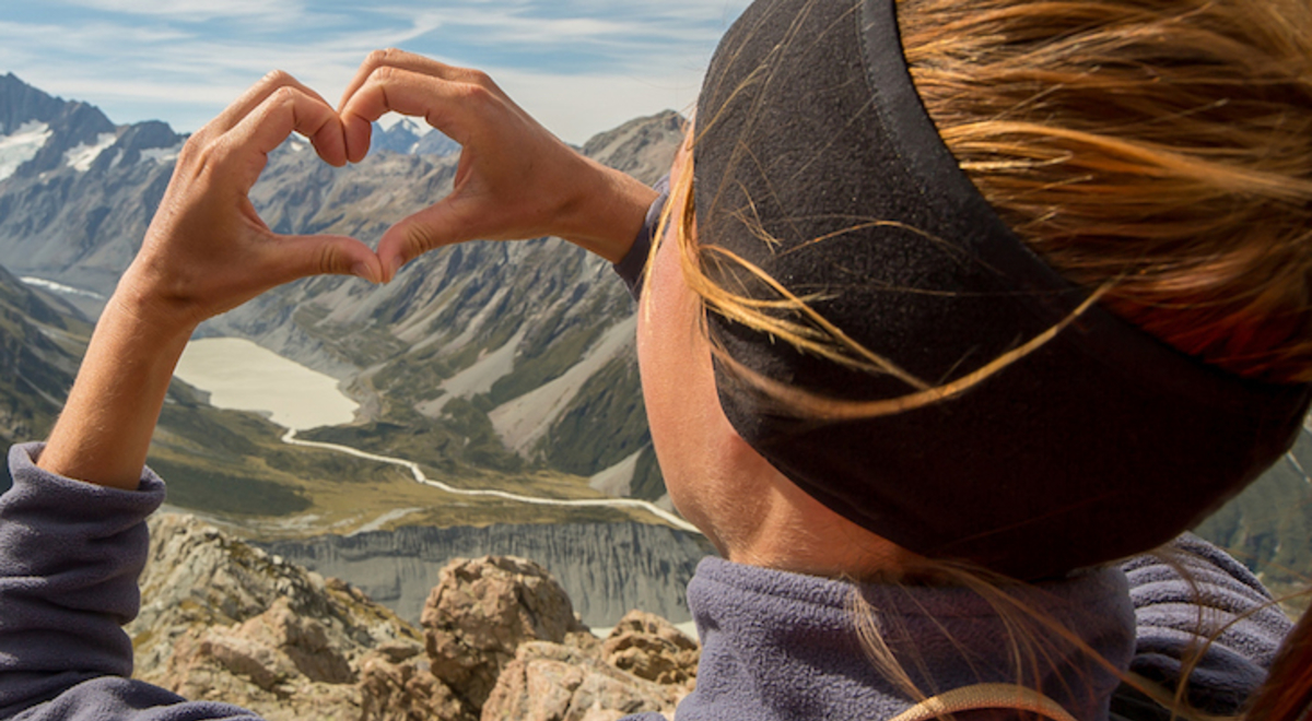 Woman looking towards the mountains making the shape of a heart with her hands 