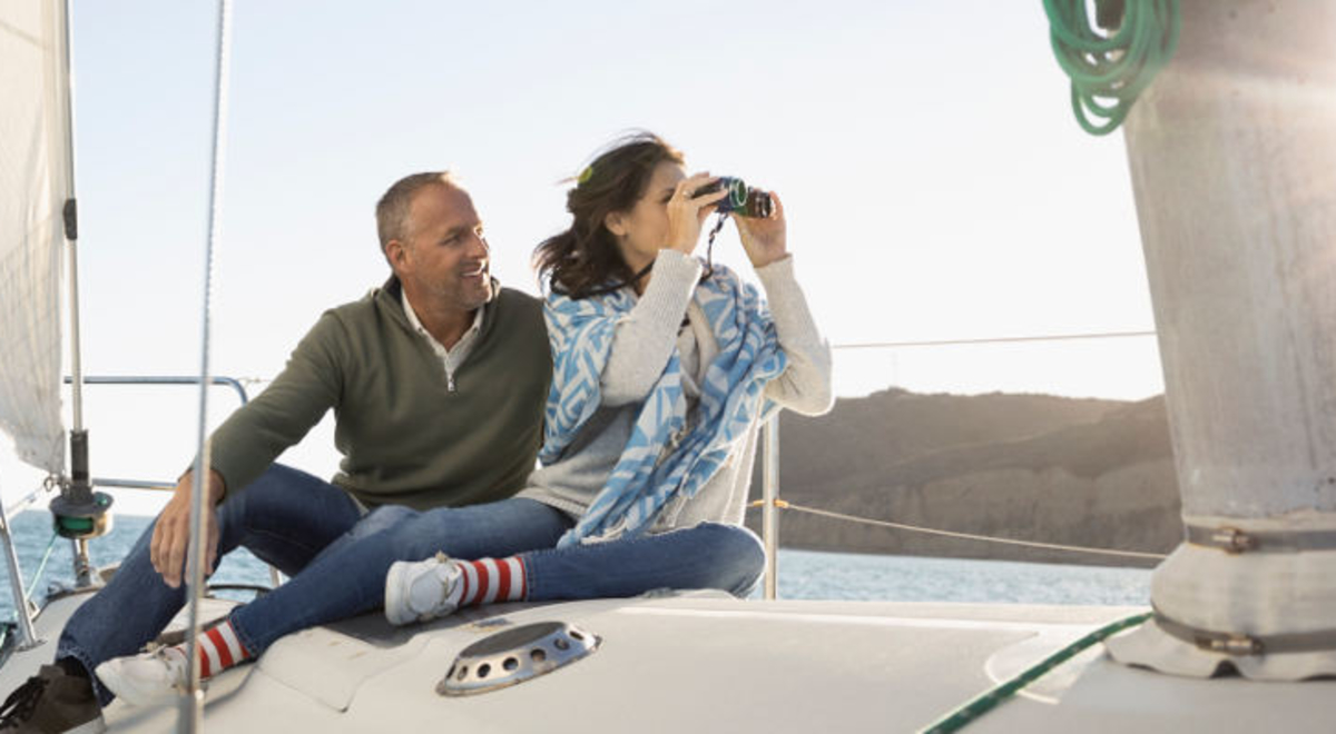 a couple riding a yacht with the woman looking through the binoculars 