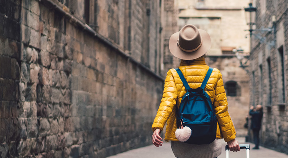 Tourist wearing a yellow puff jacket carrying a luggage walking down an alley