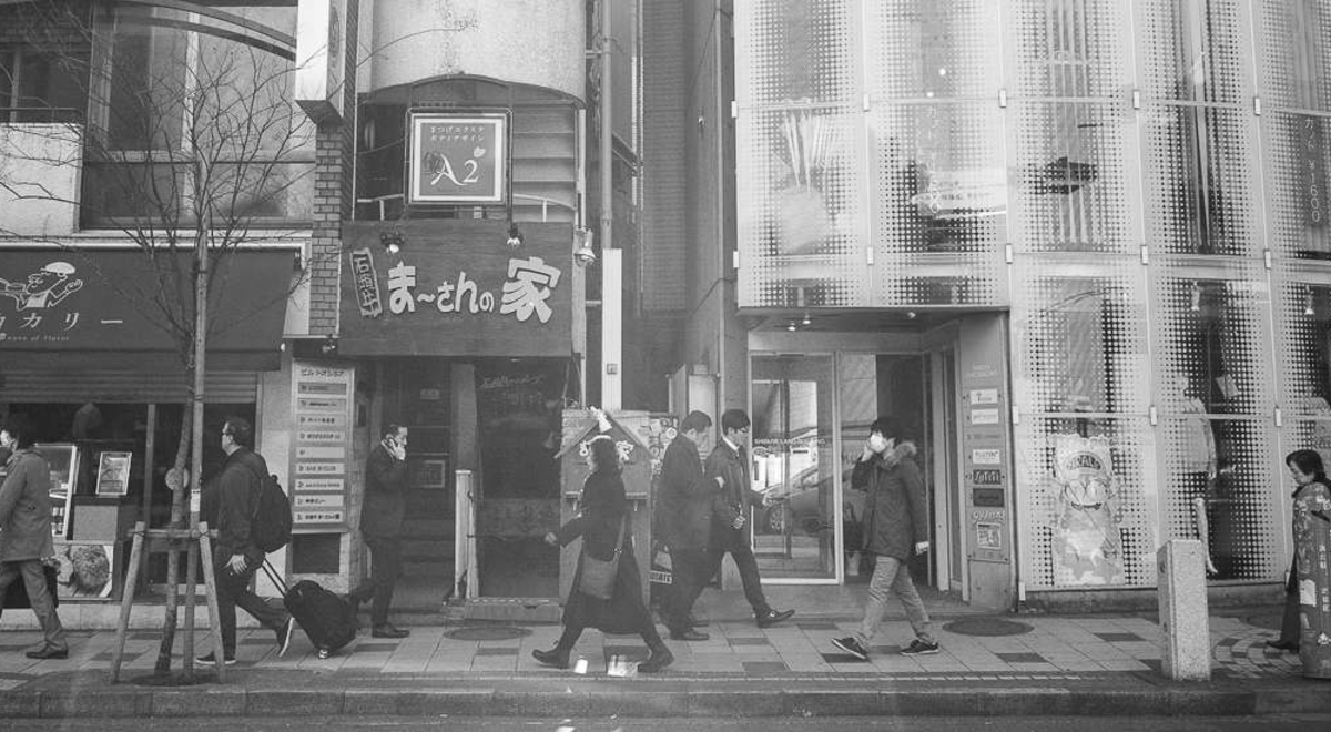 Black and white photo of pedestrians walking past the buildings in Tokyo