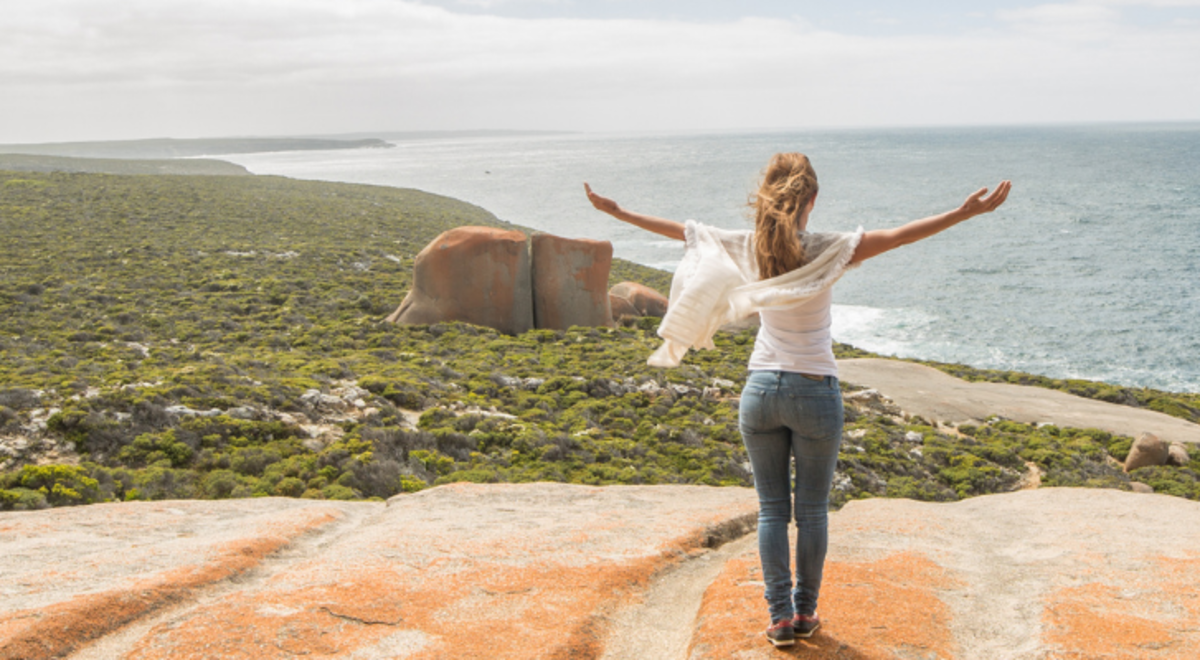 Tourist woman standing on a rock with the view of greens and ocean