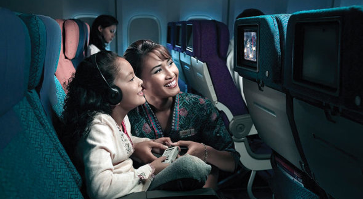 A malaysia Airline flight attendant assisting a curly liitle girl who wants to watch on the led screen at the back of the seat in front of her