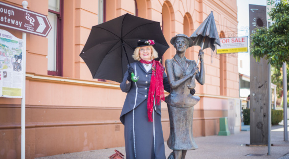 A lady holding a black umbrella and standing beside a lady statue with umbrella