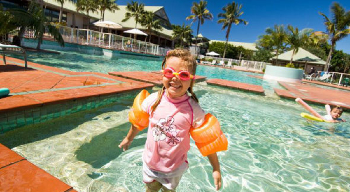 a blonde littel girl in pink shirt and orange floaters enjoying the pool in the Novotel twin waters resort