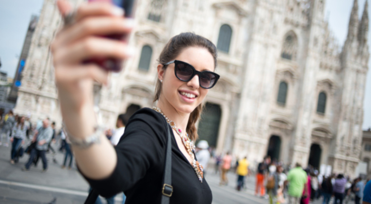 Lady smiling and taking selfie with the Duomo di Milano from behind in Milan, Italy