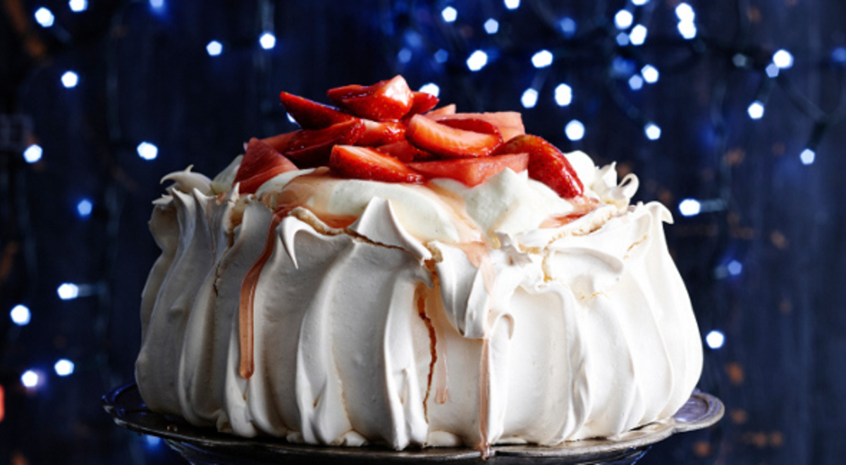 Large, strawberry-topped pavlova on a plate surrounded by small blue lights