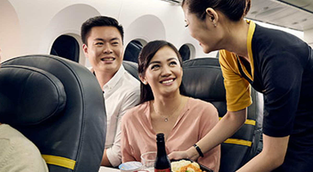 A man and a woman sitting in business class on Scoot, being served some food and drinks