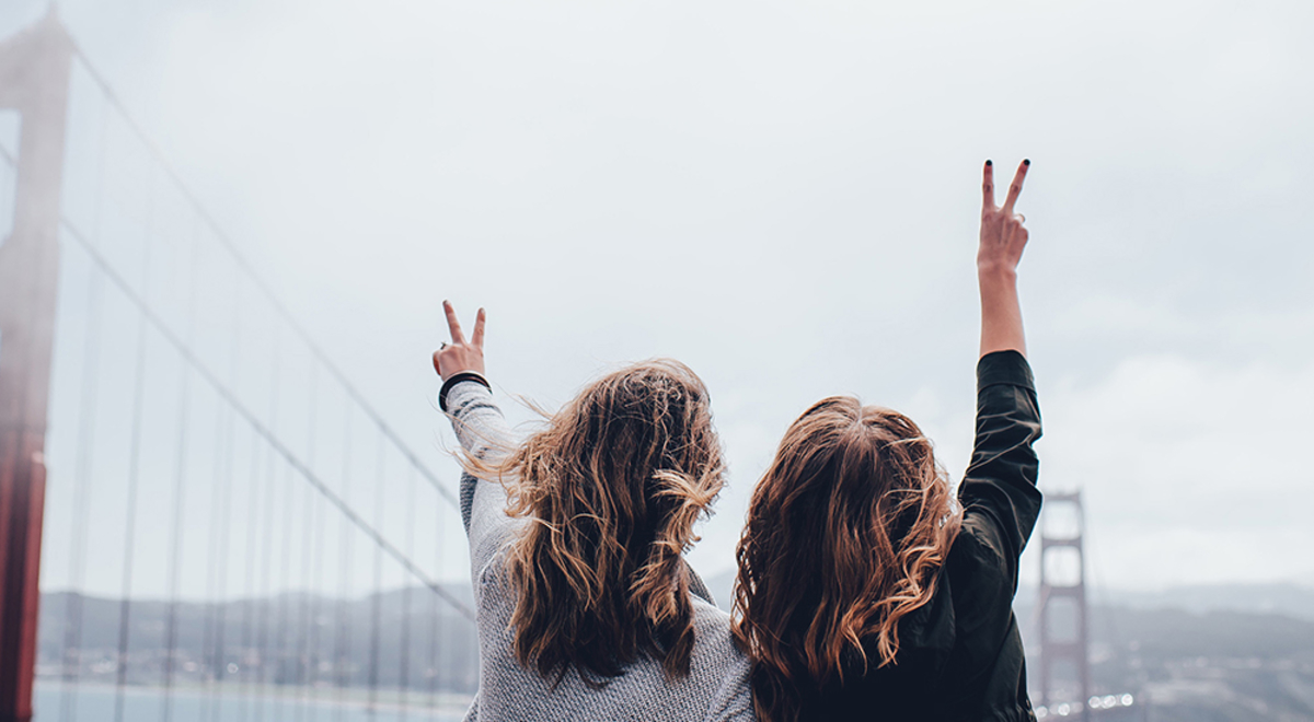 two female friend holding up a peace sign while looking at the bridge