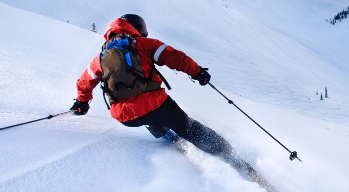 Man in a red winter jacket skiing down the snowy mountain