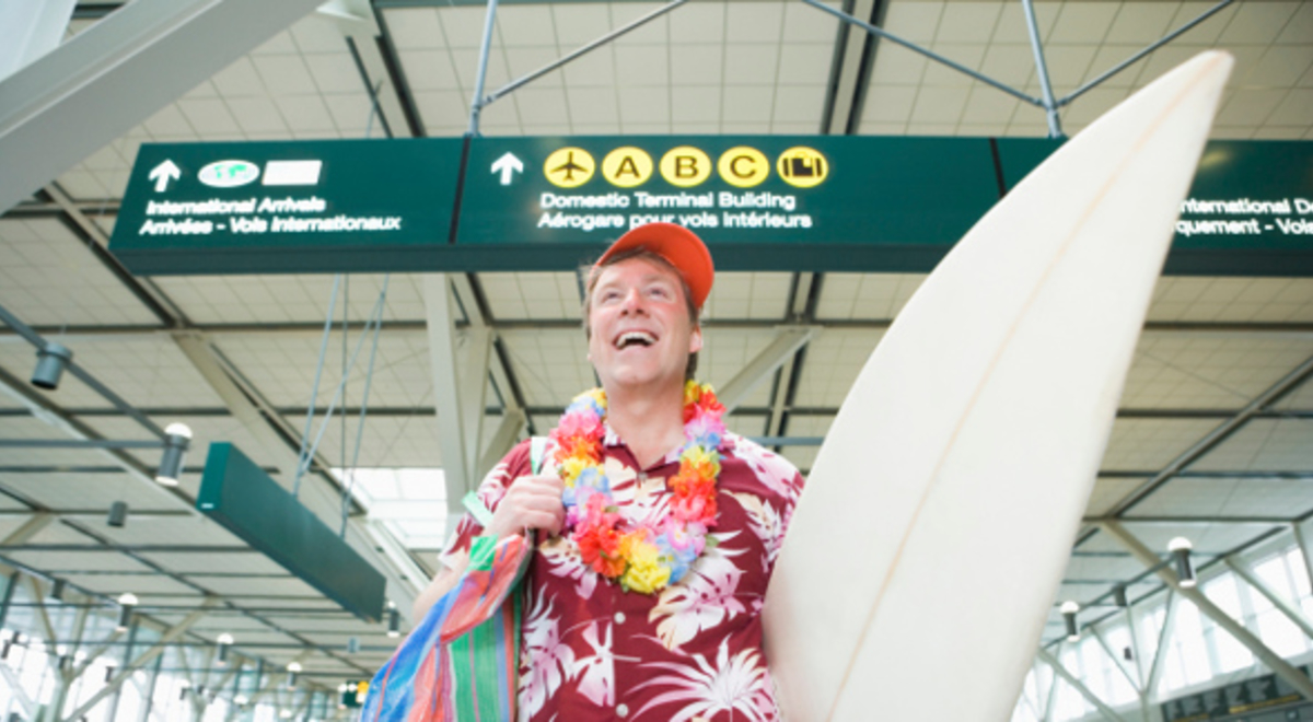 Excited traveller at the airport wearing a lei and holding a surf board 